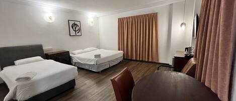 A hotel room with two beds, a dining table, a desk, and a large window with curtains.