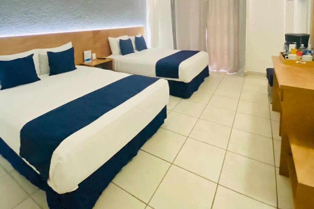 Habitación de hotel con dos camas, un escritorio y una ventana con cortinas.