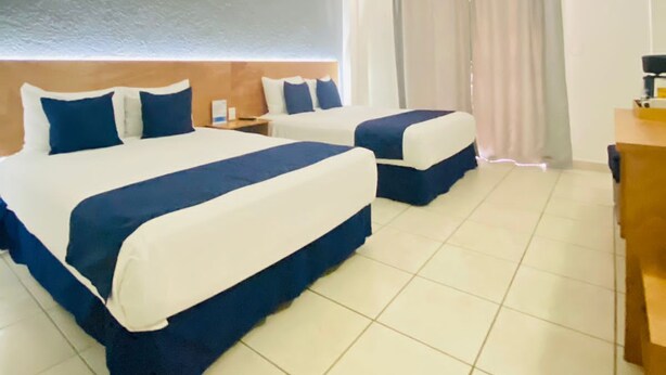 Habitación de hotel con dos camas, un escritorio y una ventana con cortinas.