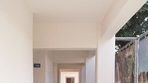 Un pasillo con suelo de baldosas, un cartel que indica la habitación 105 y una barandilla metálica a la derecha.