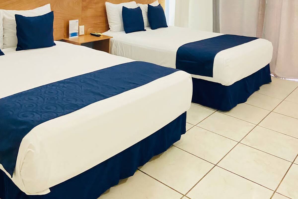 Habitación de hotel con dos camas, cabecera de madera, mesita de noche y ventana con cortinas.