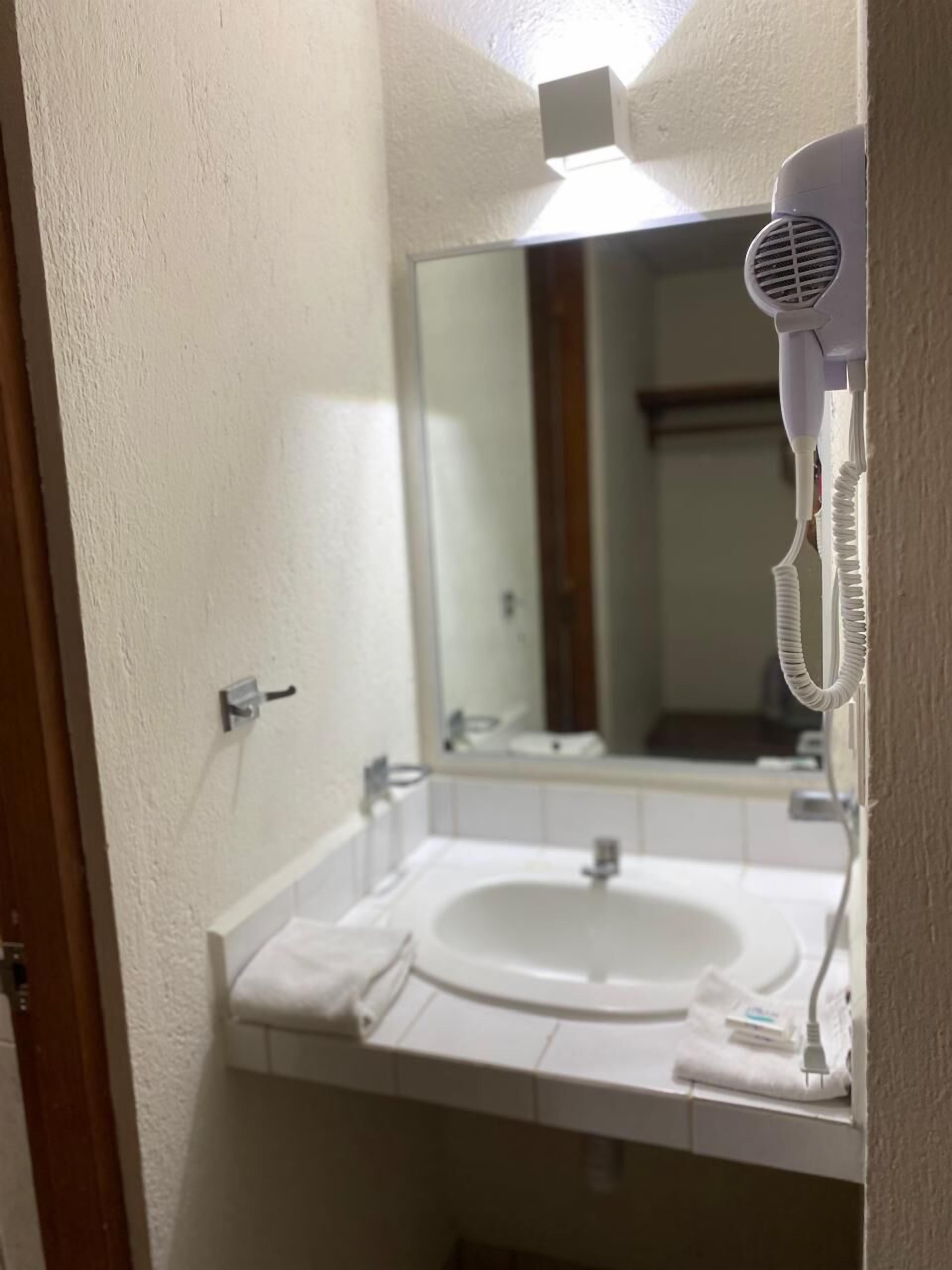 Une salle de bain avec un lavabo blanc, un miroir et un sèche-cheveux fixé au mur.