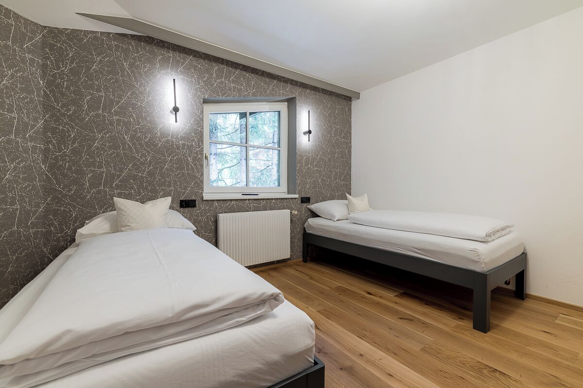 A bedroom with two beds, a window, and a radiator.
