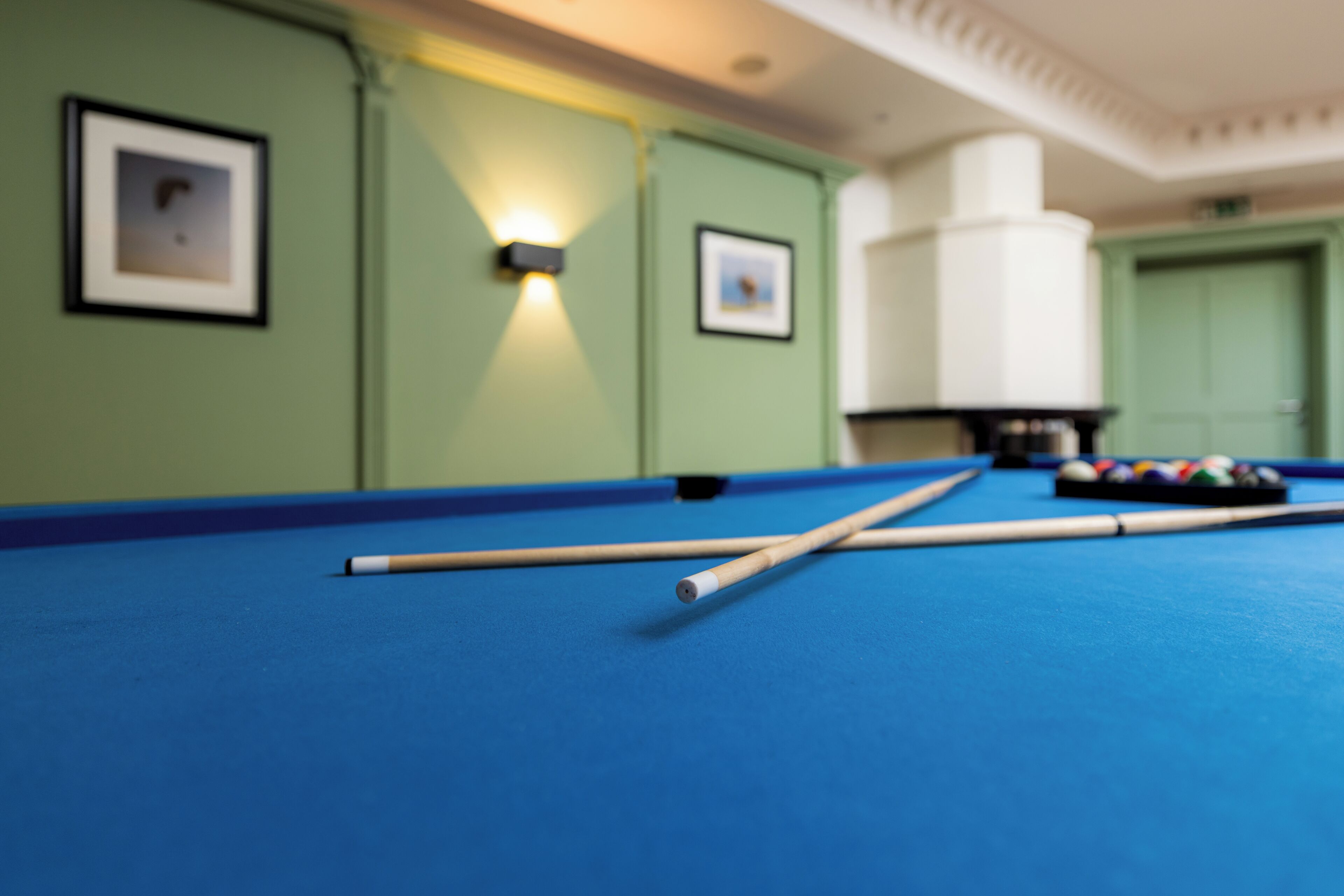 A pool table with pool cues, a framed picture on the wall, and a white pillar.
