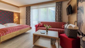 Habitación de hotel con cama, sofá, mesa de centro, televisor y ventana con cortinas.
