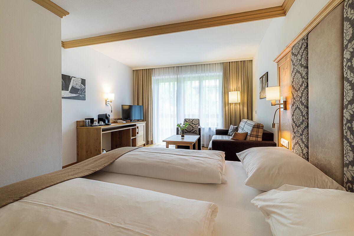 A hotel room with two beds, a desk, a chair, a sofa, and a TV.