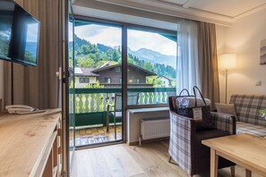 Ein Zimmer mit einem Holztisch, einer Couch, einem Fernseher und einem Balkon mit Bergblick.