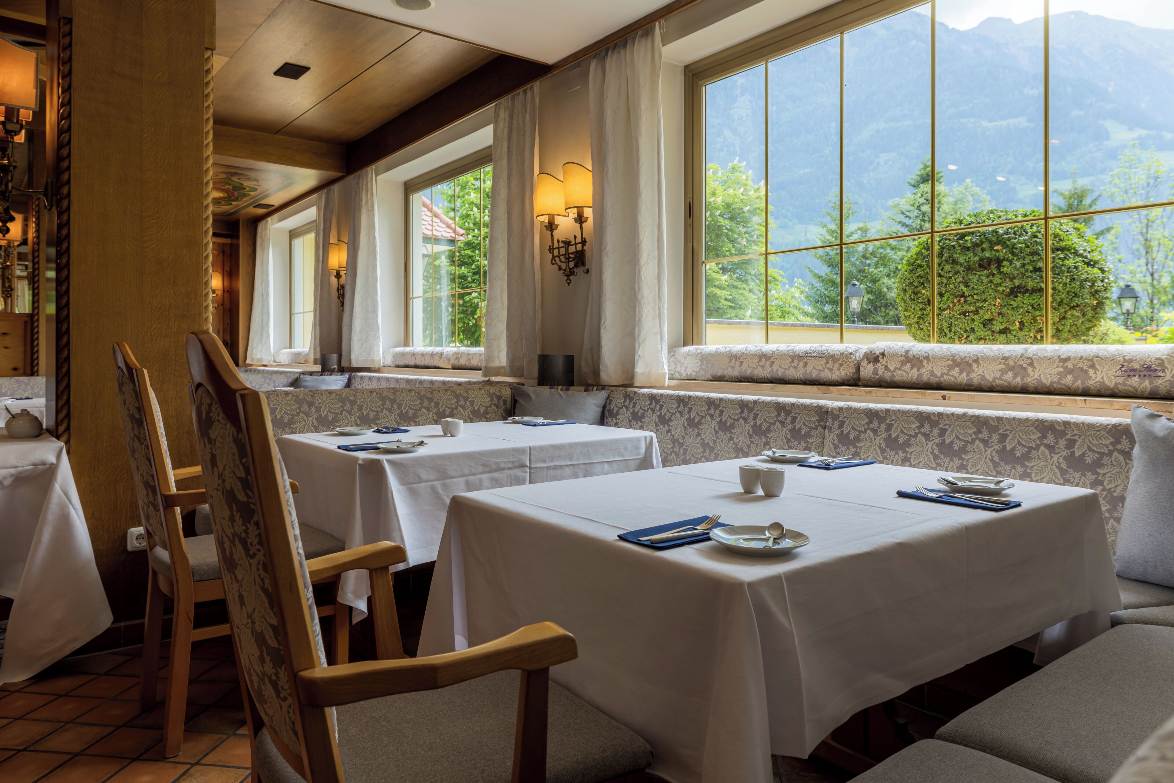 A restaurant with tables set for dining, large windows with mountain views, and a cozy interior.