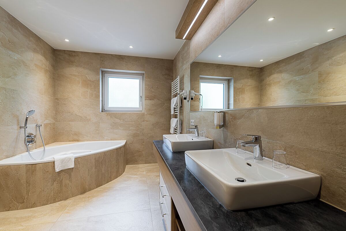 Un baño moderno con bañera, dos lavamanos, un espejo grande y una ventana.