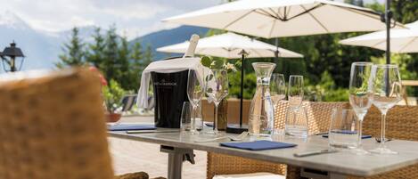 A table set outdoors with a bottle of Moët & Chandon champagne, clear glasses, and a wicker chair.