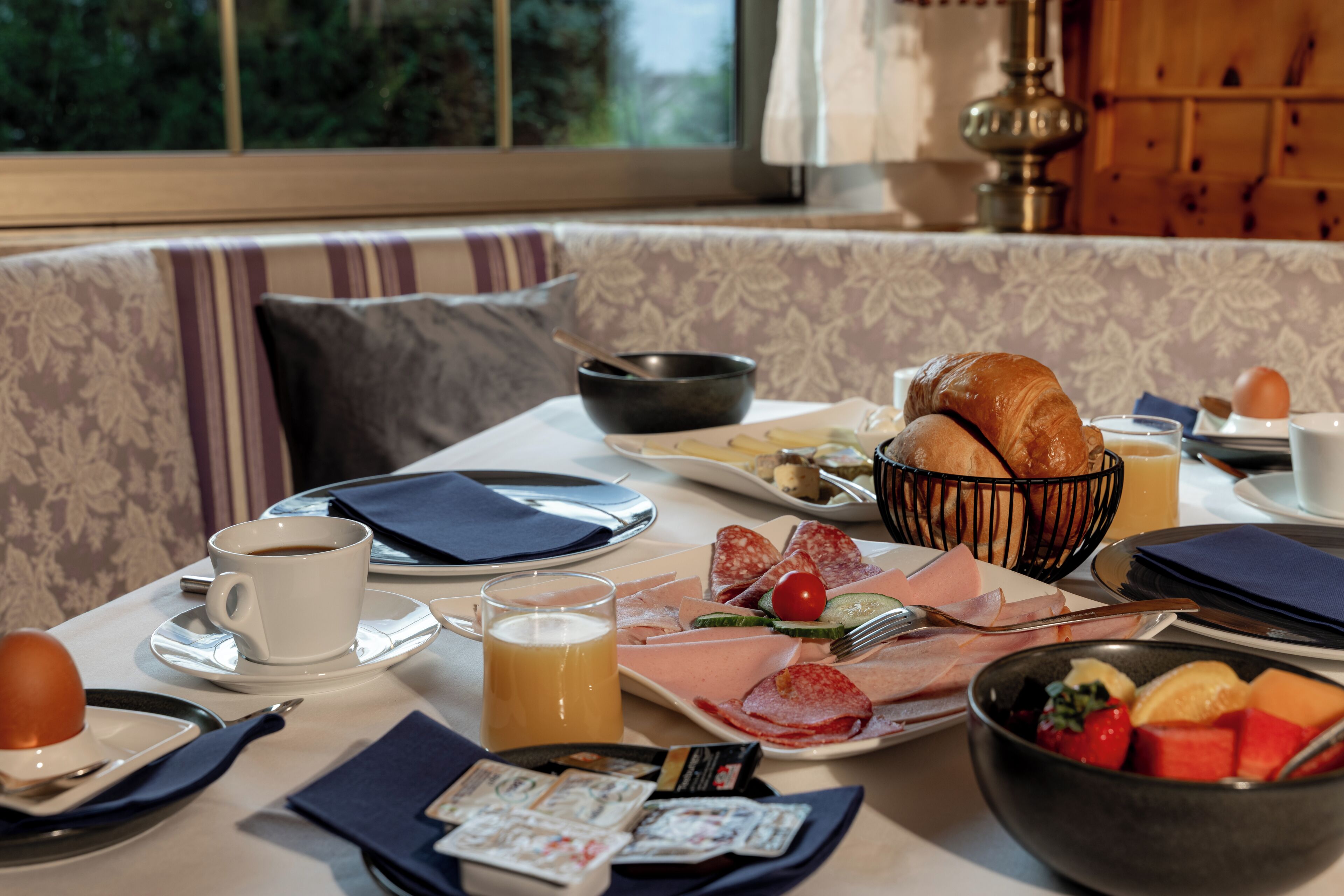 A breakfast setting with a table, plates, bowls, and a window view.