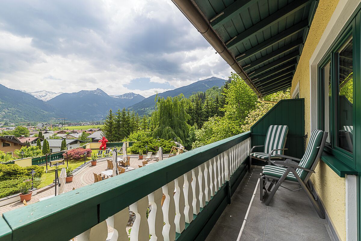 A balcony with a view of mountains, a railing, and two striped chairs.