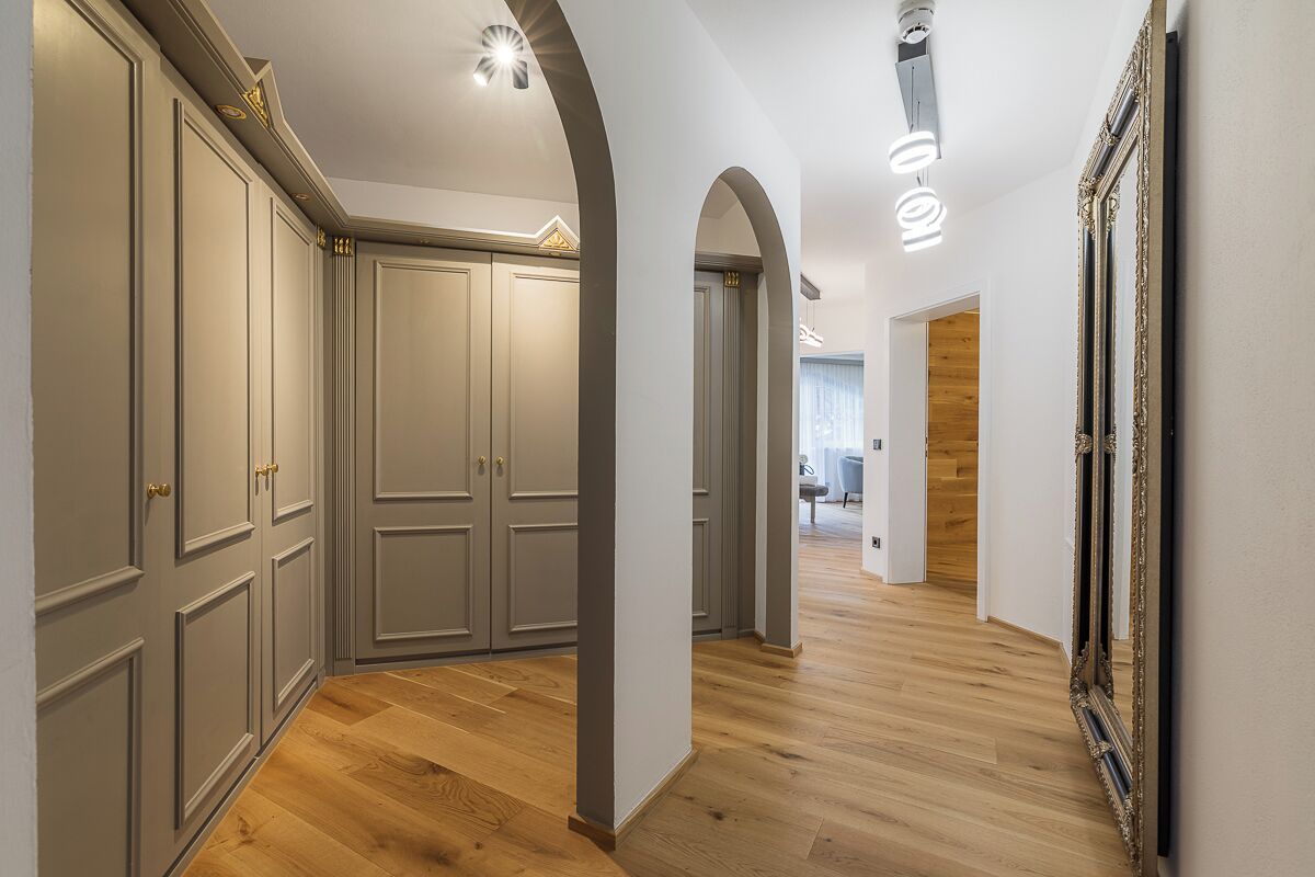 A hallway with wooden flooring, grey cabinets, and a large mirror on the right.