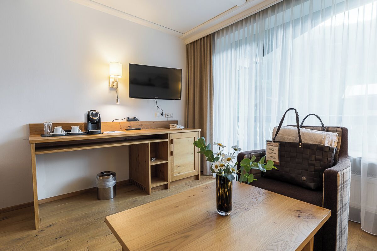 A hotel room with a wooden desk, a television, a sofa, and a coffee machine.
