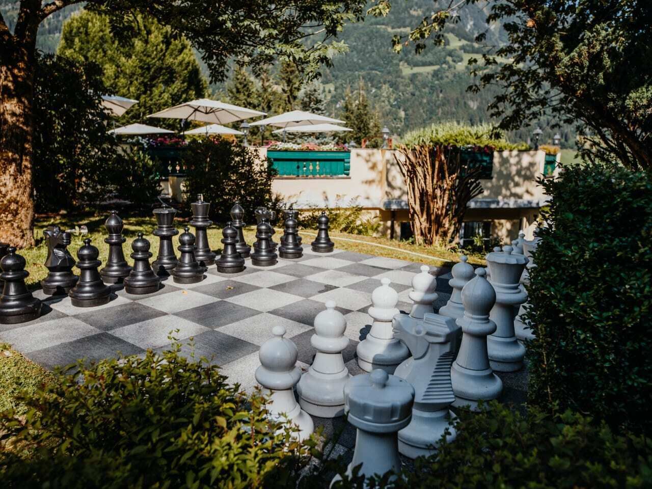 A large outdoor chessboard surrounded by greenery and umbrellas.