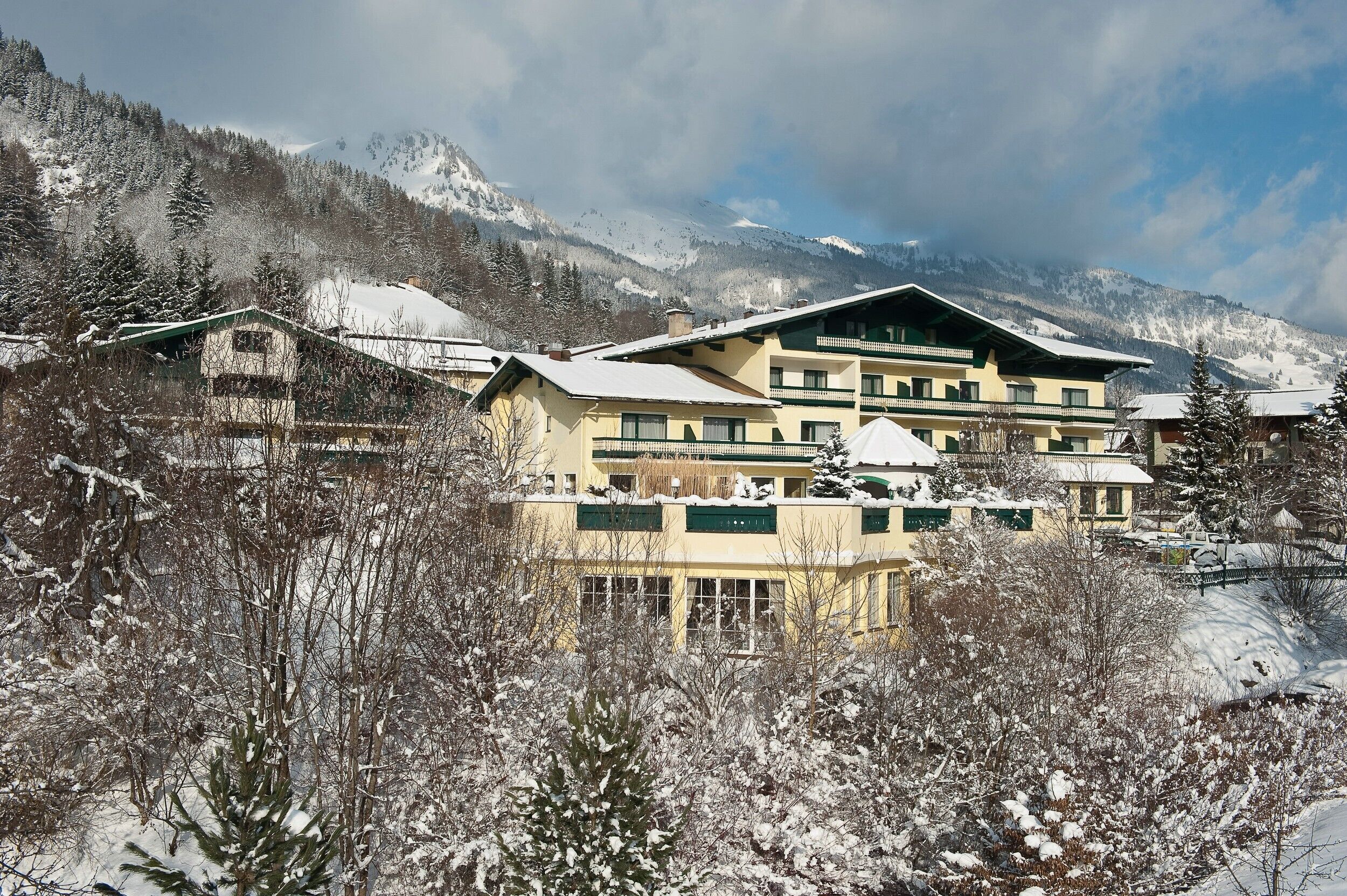 Ein mehrstöckiges Hotel mit verschneitem Dach, umgeben von schneebedeckten Bäumen und Bergen im Hintergrund.