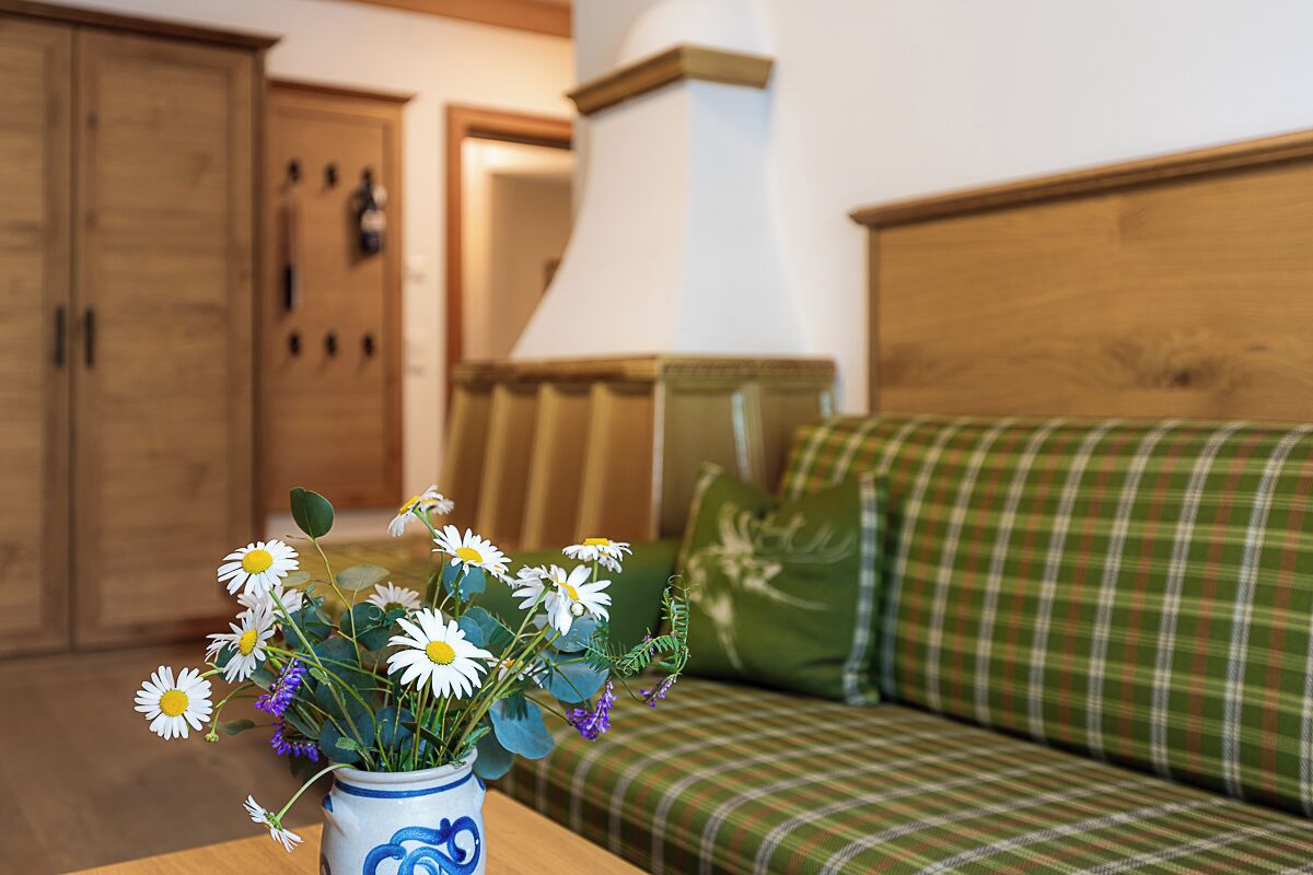 Una habitación con un armario de madera, un sofá escocés y un florero con flores sobre una mesa.