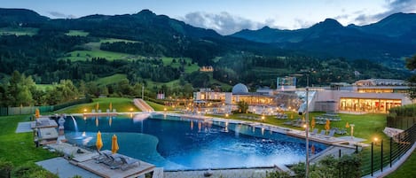 A resort with a large swimming pool, lounge areas, and a view of the surrounding mountains.