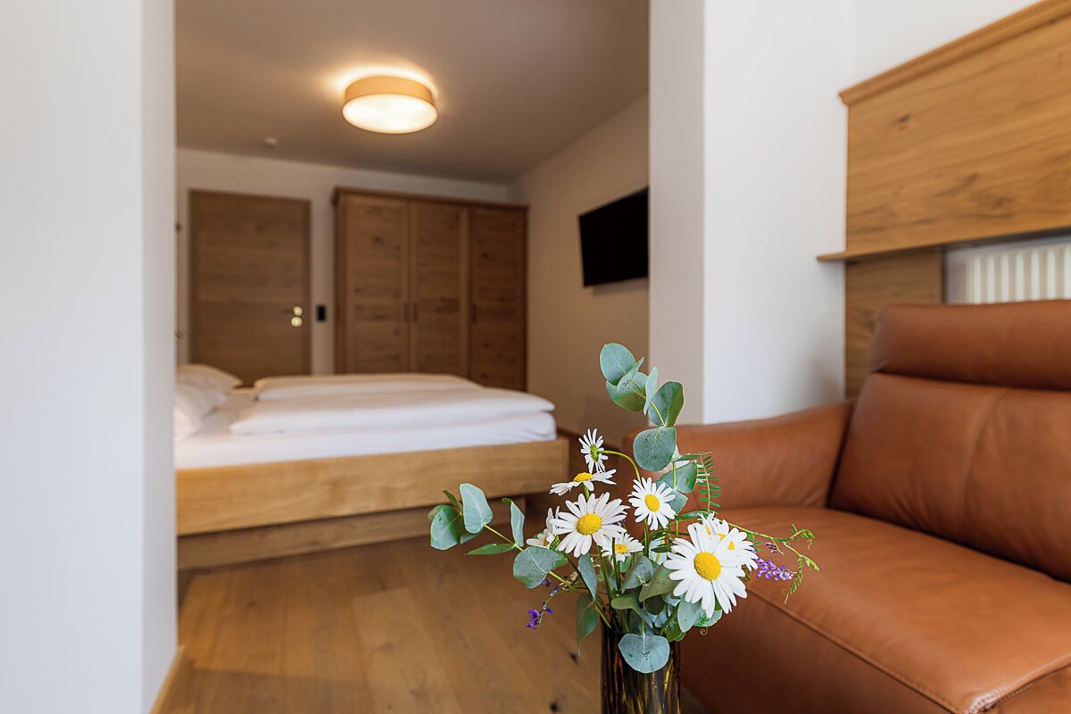 A bedroom with a bed, wooden wardrobe, and a brown leather sofa.