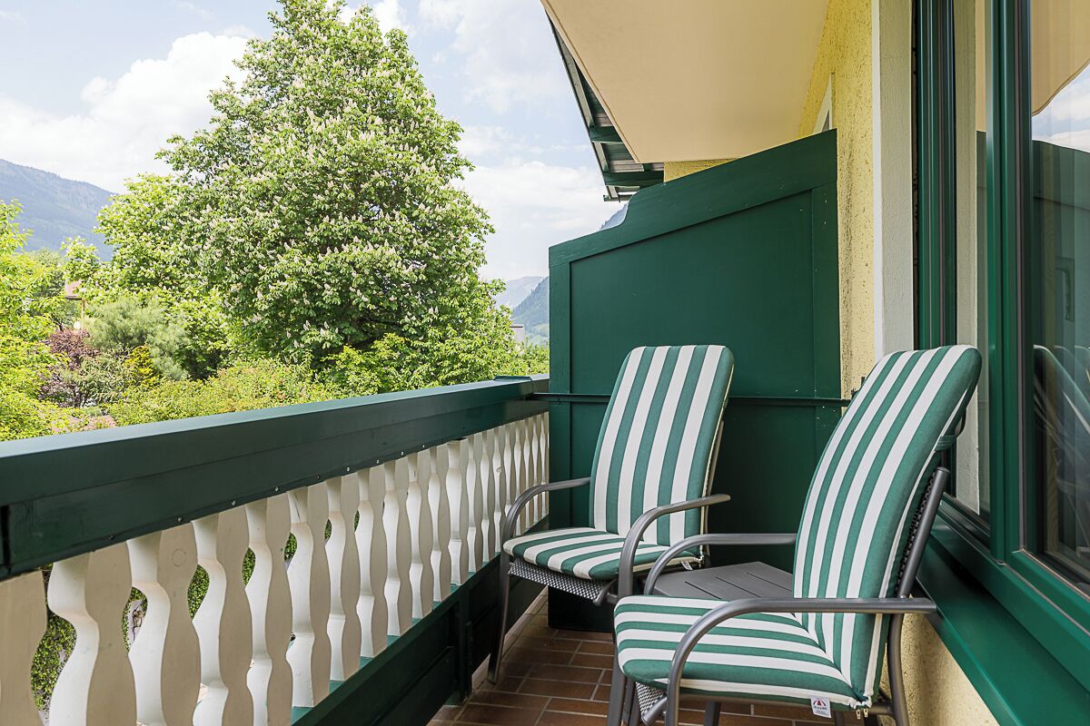 Un balcon avec deux chaises à rayures, une balustrade blanche et une vue sur la verdure et les montagnes.