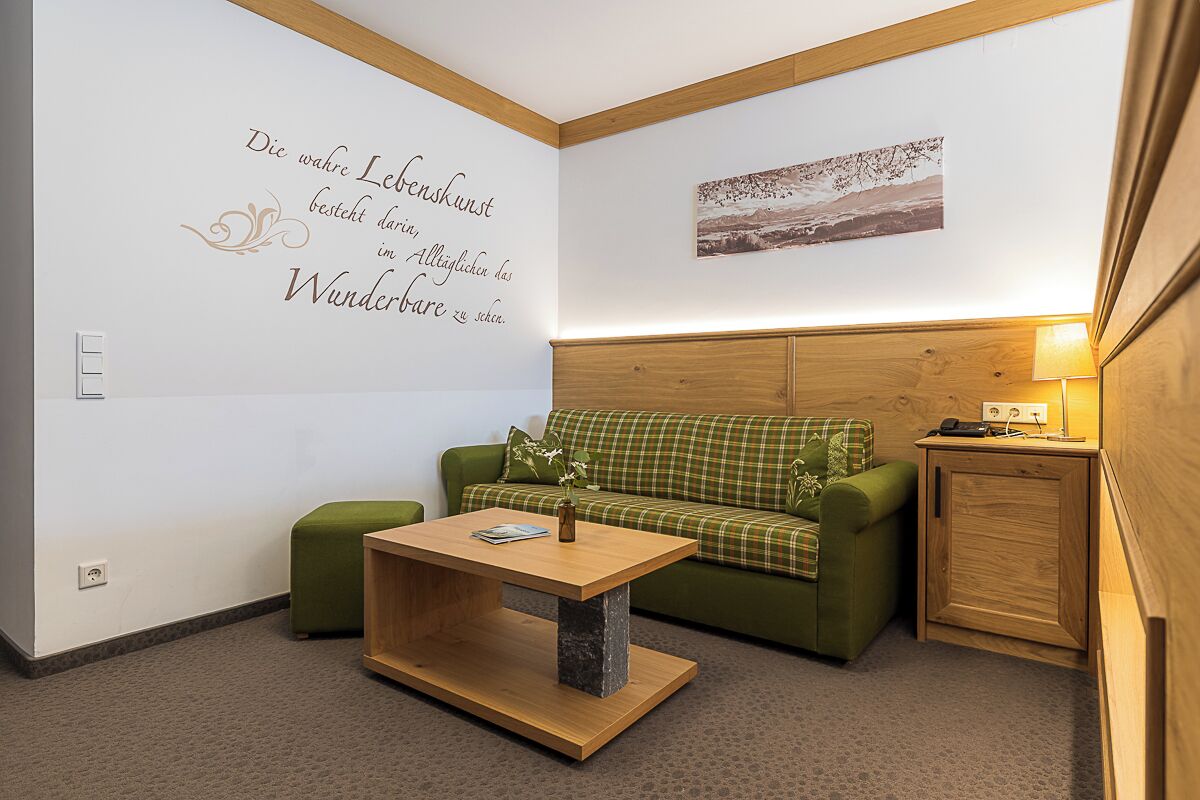 A room with a green sofa, a wooden coffee table, a wall-mounted picture, and a small wooden cabinet.