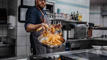 Una persona friendo comida en una cocina comercial, con una estufa a gas y diverso equipamiento de cocina.
