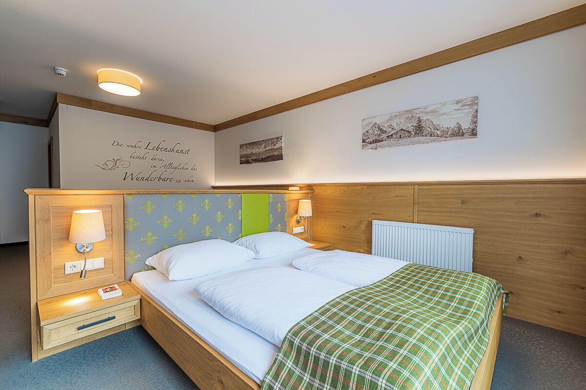 A bedroom with a bed, bedside tables, wall art, and a wooden headboard.