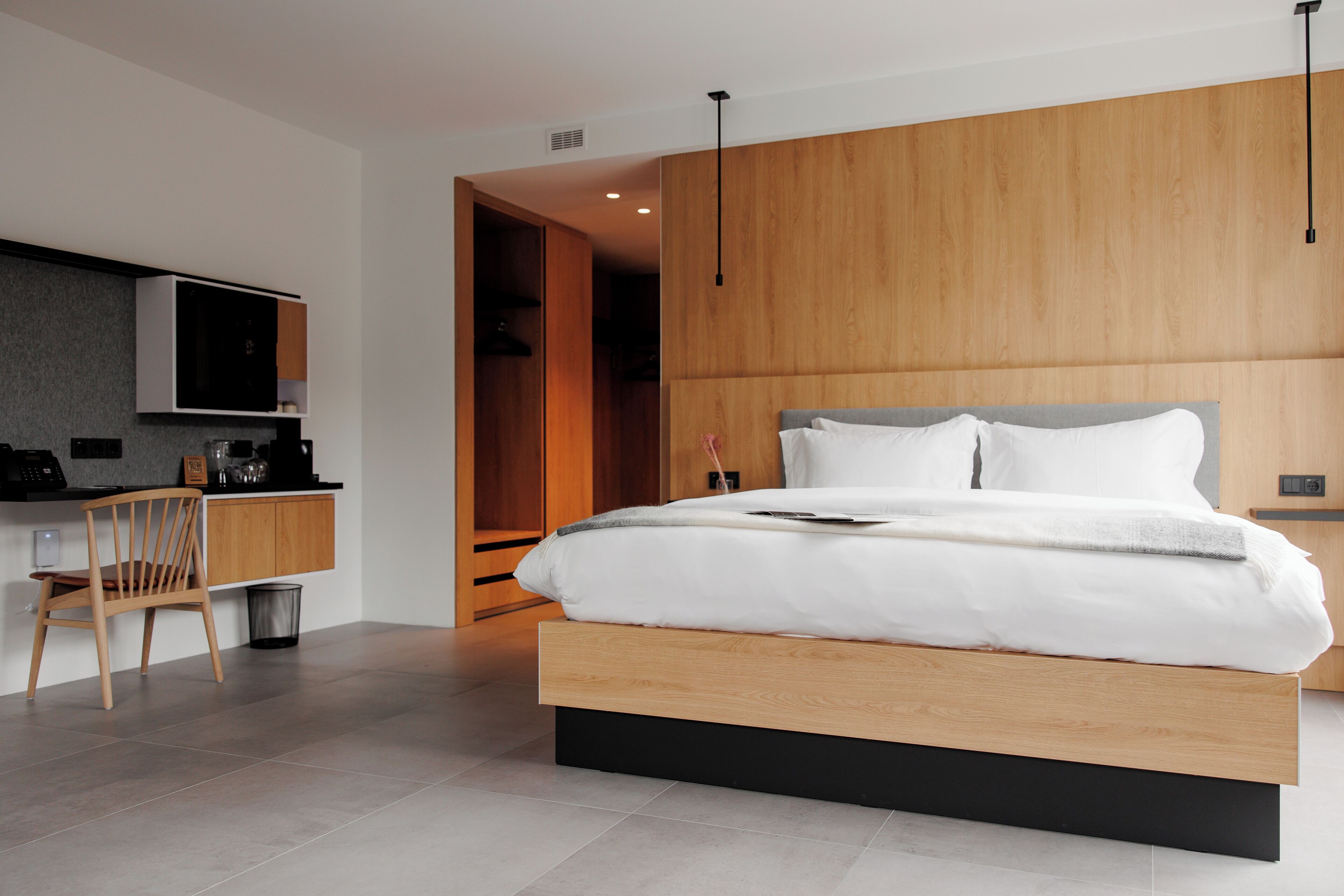 A modern bedroom with a wooden bed frame, a built-in desk, and a chair.