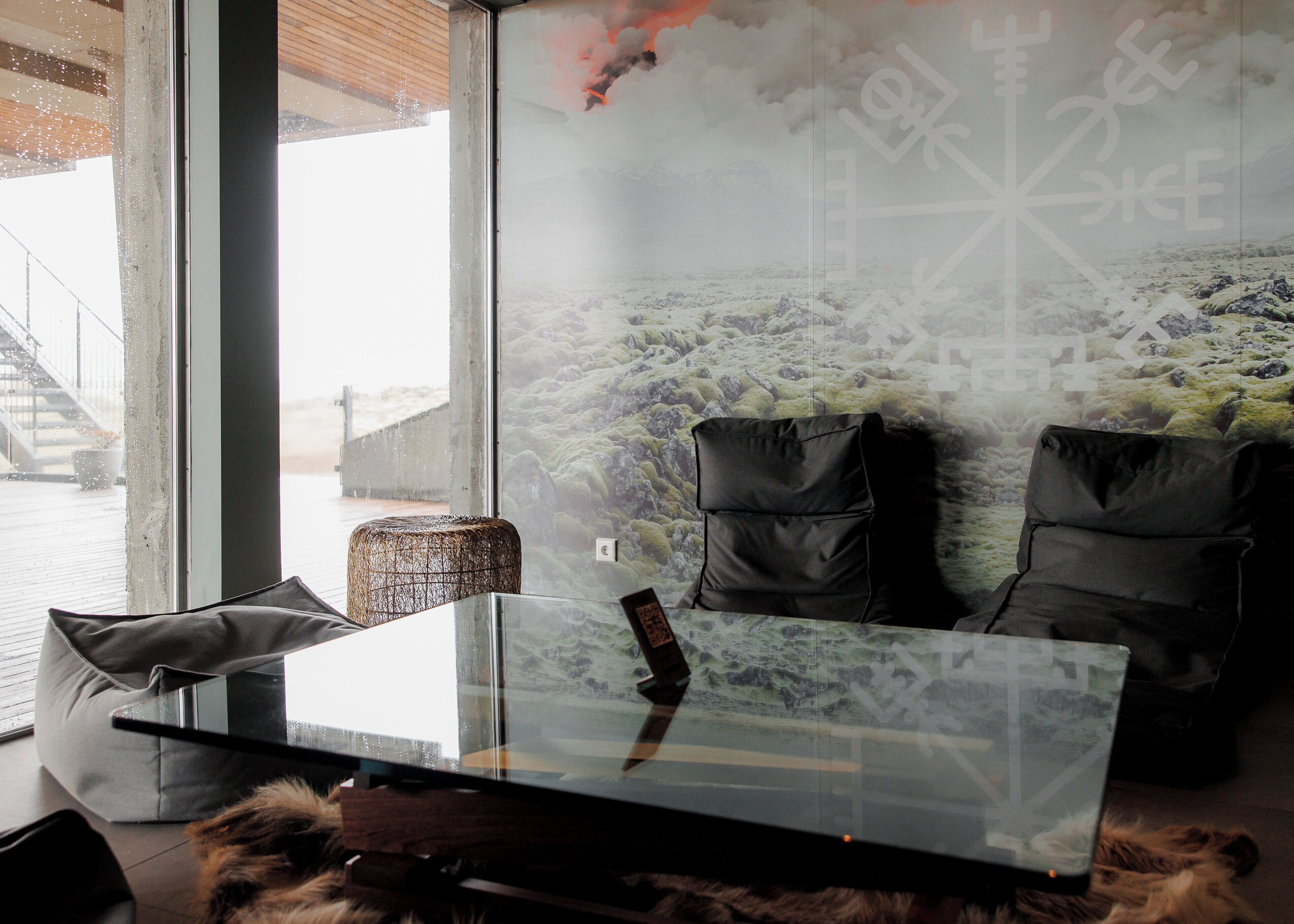 Una habitación moderna con una mesa de vidrio, dos sillas acolchadas negras, un manto de piel y un gran ventanal con vistas a un paisaje nevado.