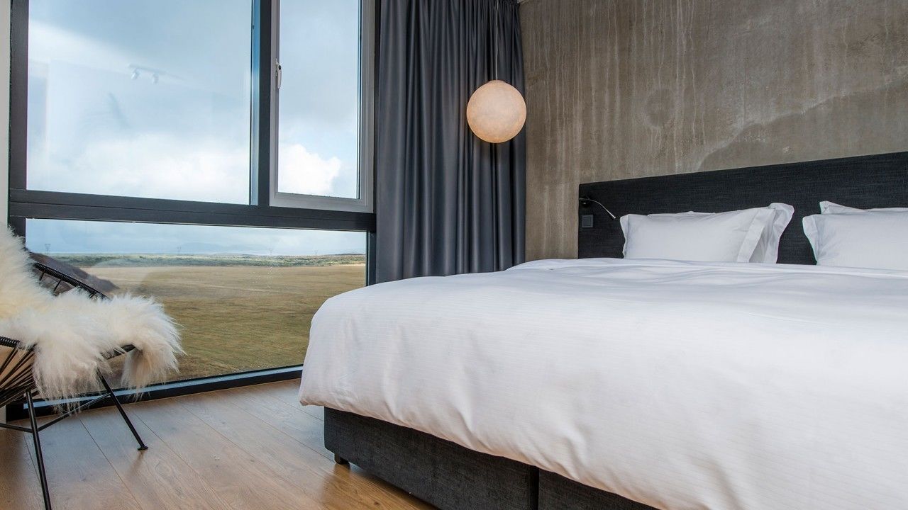 Ein modernes Schlafzimmer mit einem großen Bett, Blick auf die Landschaft und einem großen Fenster.
