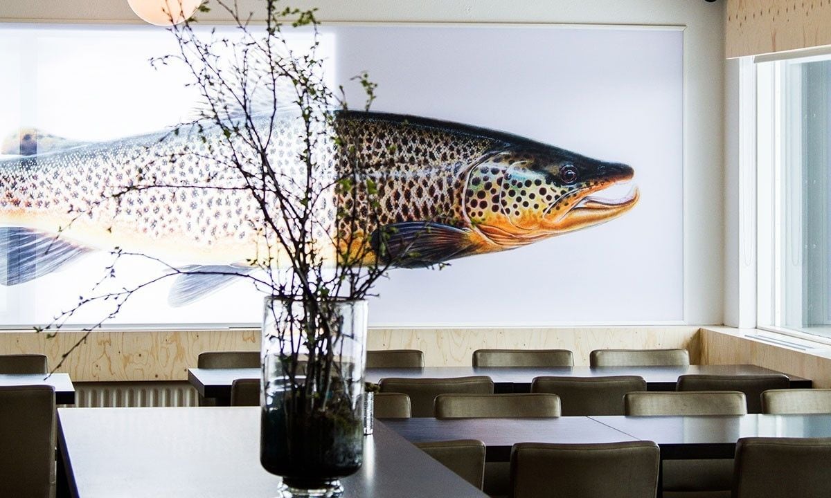 A restaurant with a large fish mural on the wall, a vase with branches, and several tables and chairs.