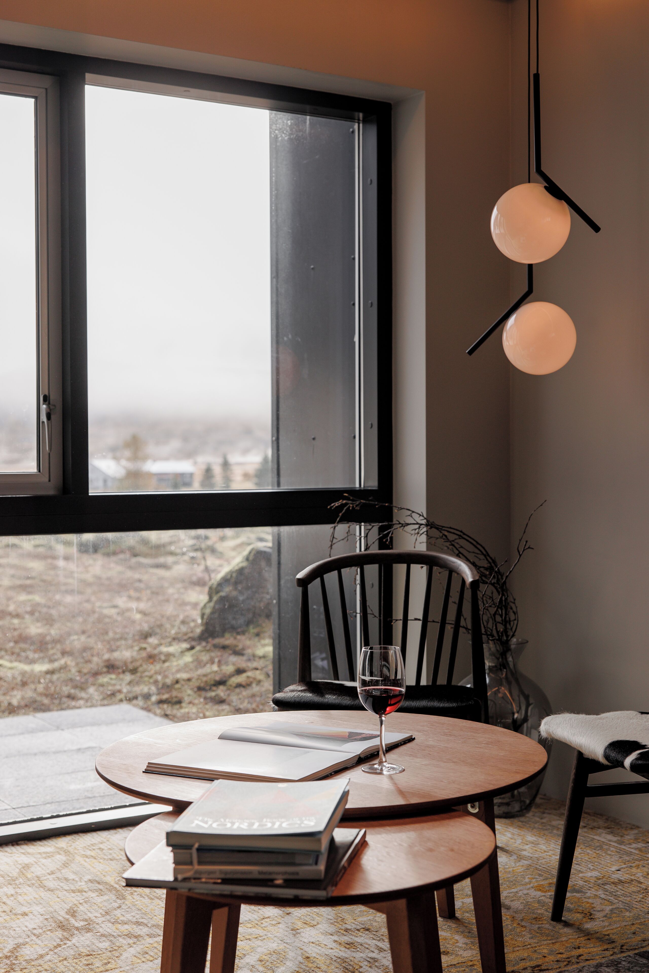 Ett mysigt rum med ett stort fönster, ett runt bord, en stol och en hängande lampa.