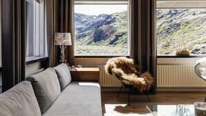 A modern living room with a sofa, a chair, a lamp, and a view of a mountainous landscape through large windows.