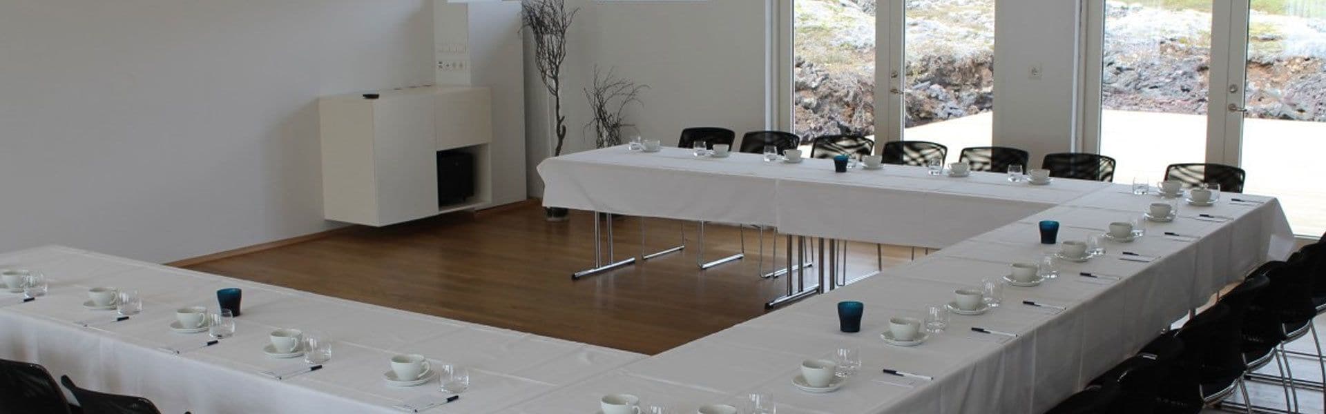 Una sala de conferències amb dues taules llargues preparades per una reunió, equipada amb cadires i taules, i un gran finestral que ofereix vistes a l'exterior.