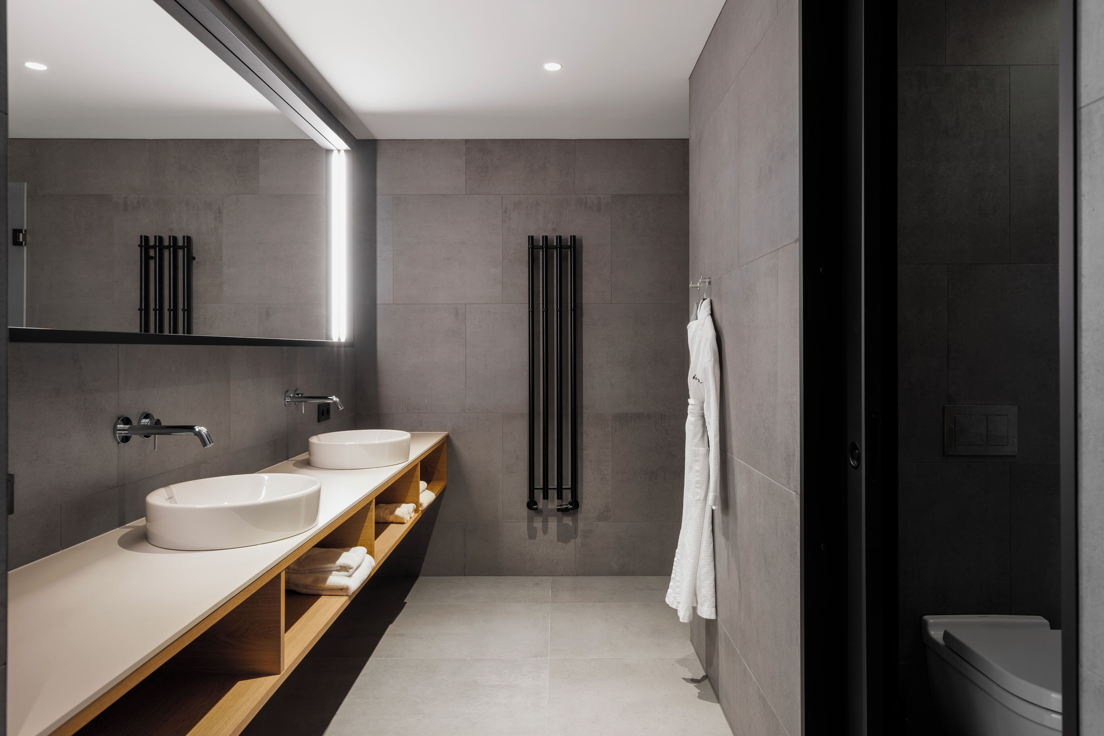 A modern bathroom with two sinks, a mirror, a towel rack, and a shower area.