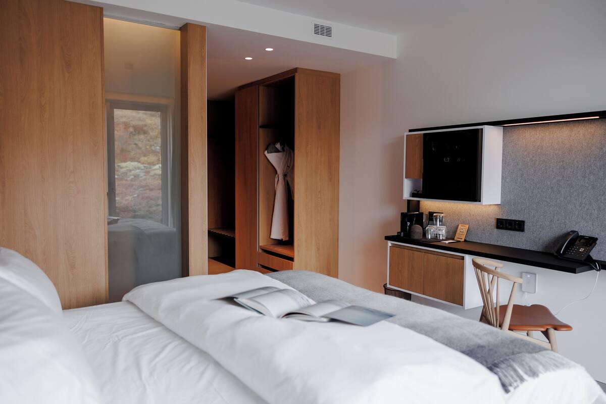 Habitación de hotel moderna con una cama grande, un armario de madera, una kitchenette y un televisor montado en la pared.