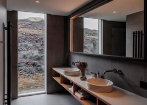 A modern bathroom with a large mirror, two sinks, and a view of a rocky landscape through the window.