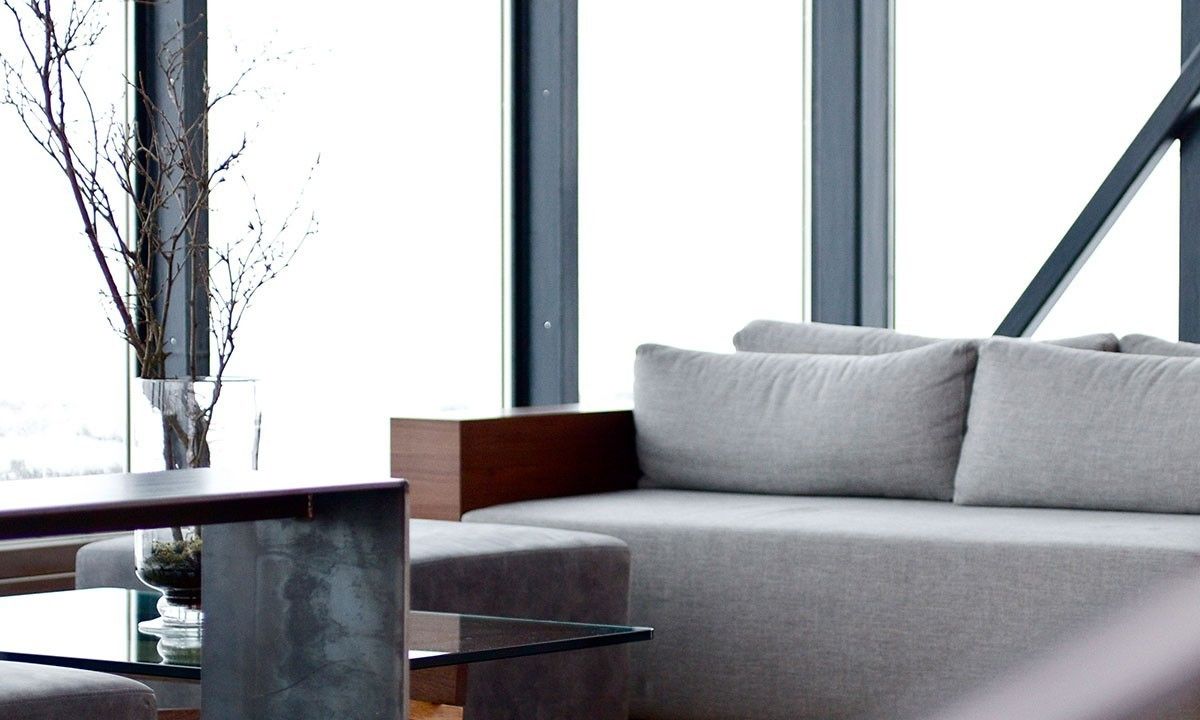 A modern living room with a grey sofa, a glass coffee table, and a vase with branches.