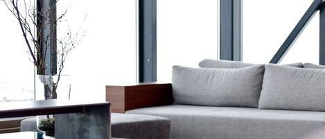 A modern living room with a grey sofa, a glass coffee table, and a vase with branches.