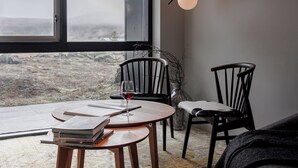 A cozy room with a large window, two chairs, a table with a wine glass, and a vase with branches.