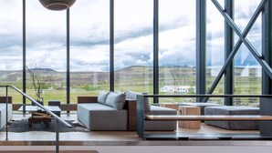 A modern interior with large windows, grey sofas, and wooden tables. - ION Adventure Hotel, Nesjavellir, a Member of Design Hotels (Selfoss)