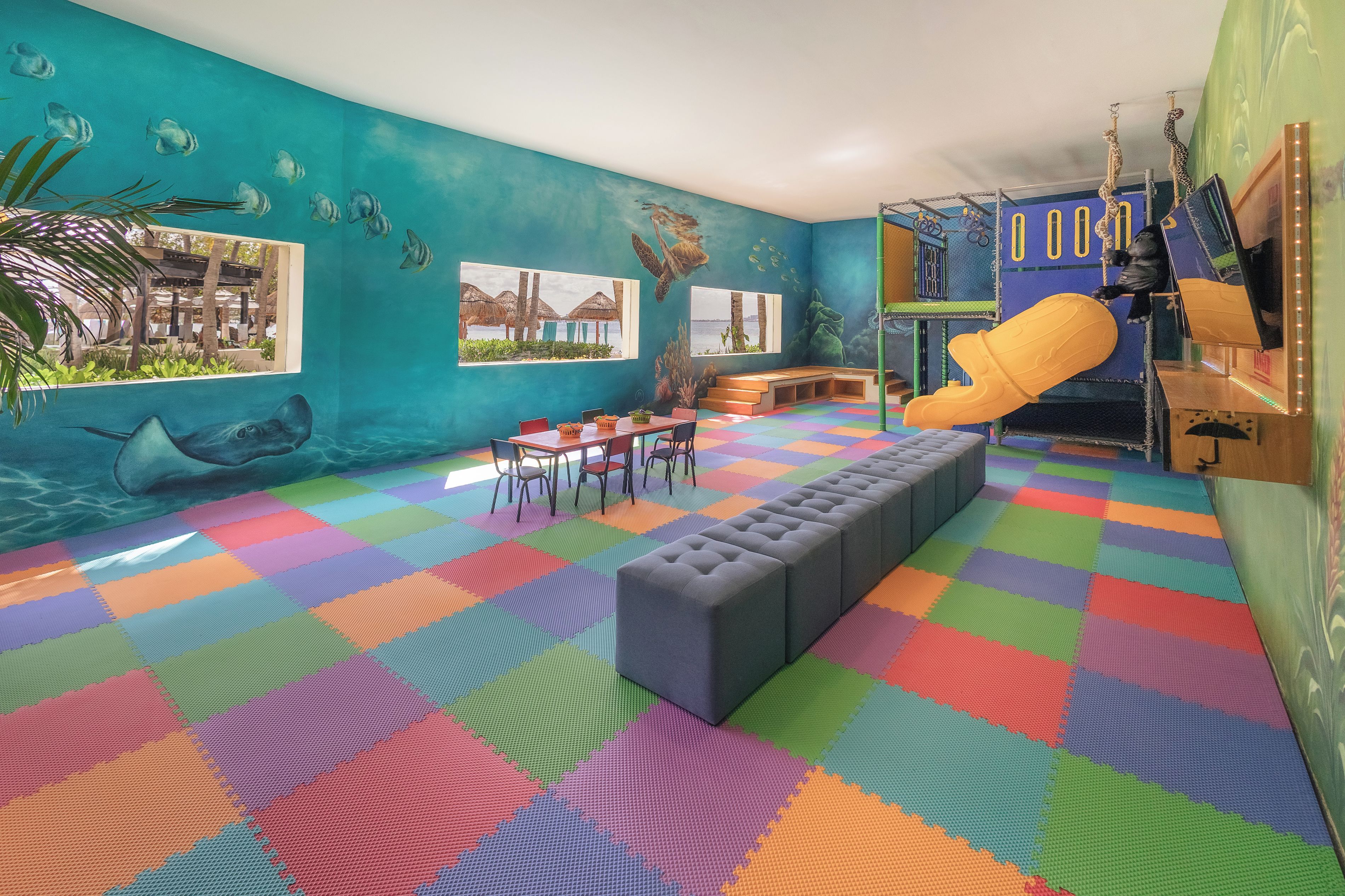 Una sala de juegos con piso de espuma de colores, un tobogán y una zona de estar.