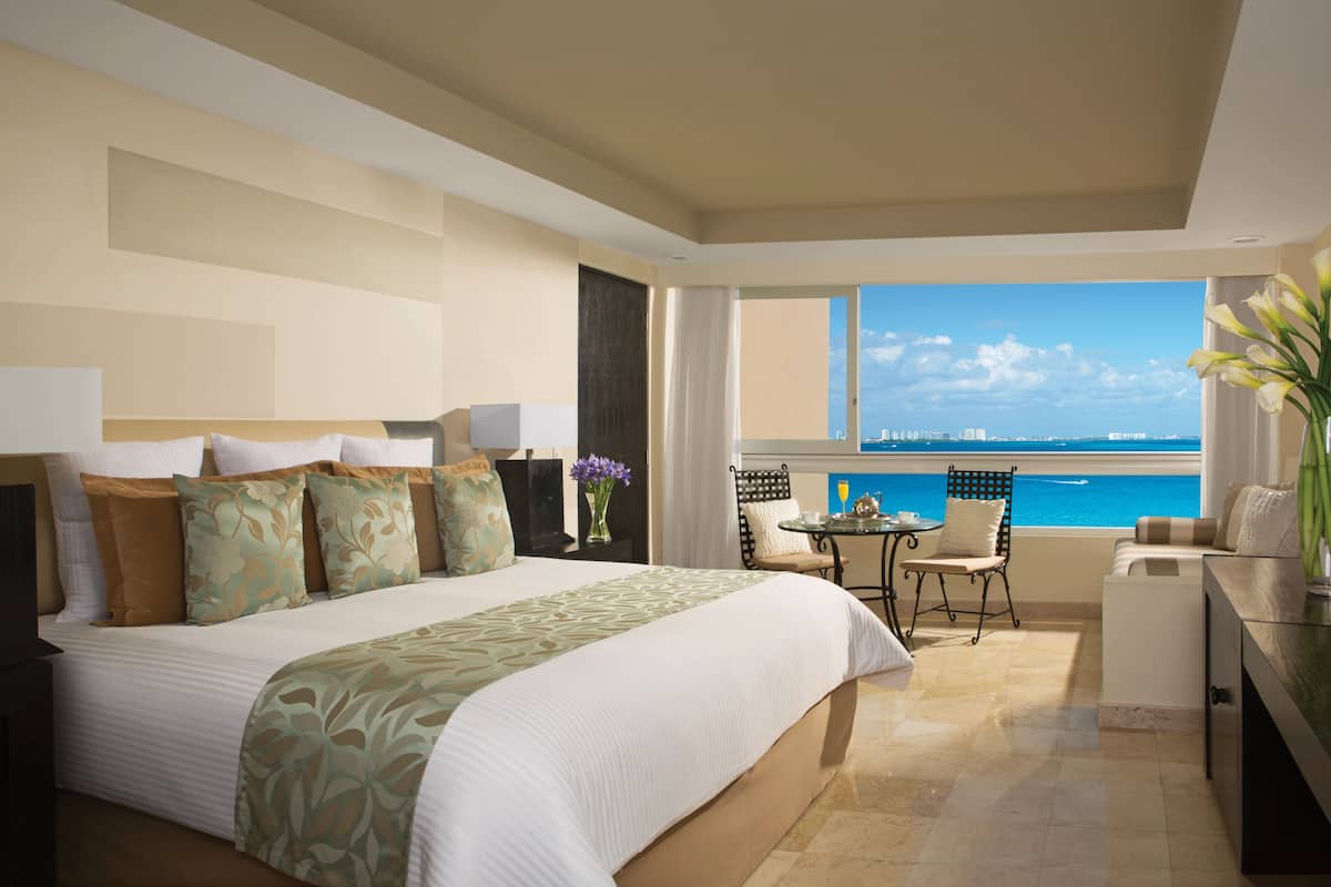 A hotel room with a large bed, a small table, a chair, and a view of the ocean.