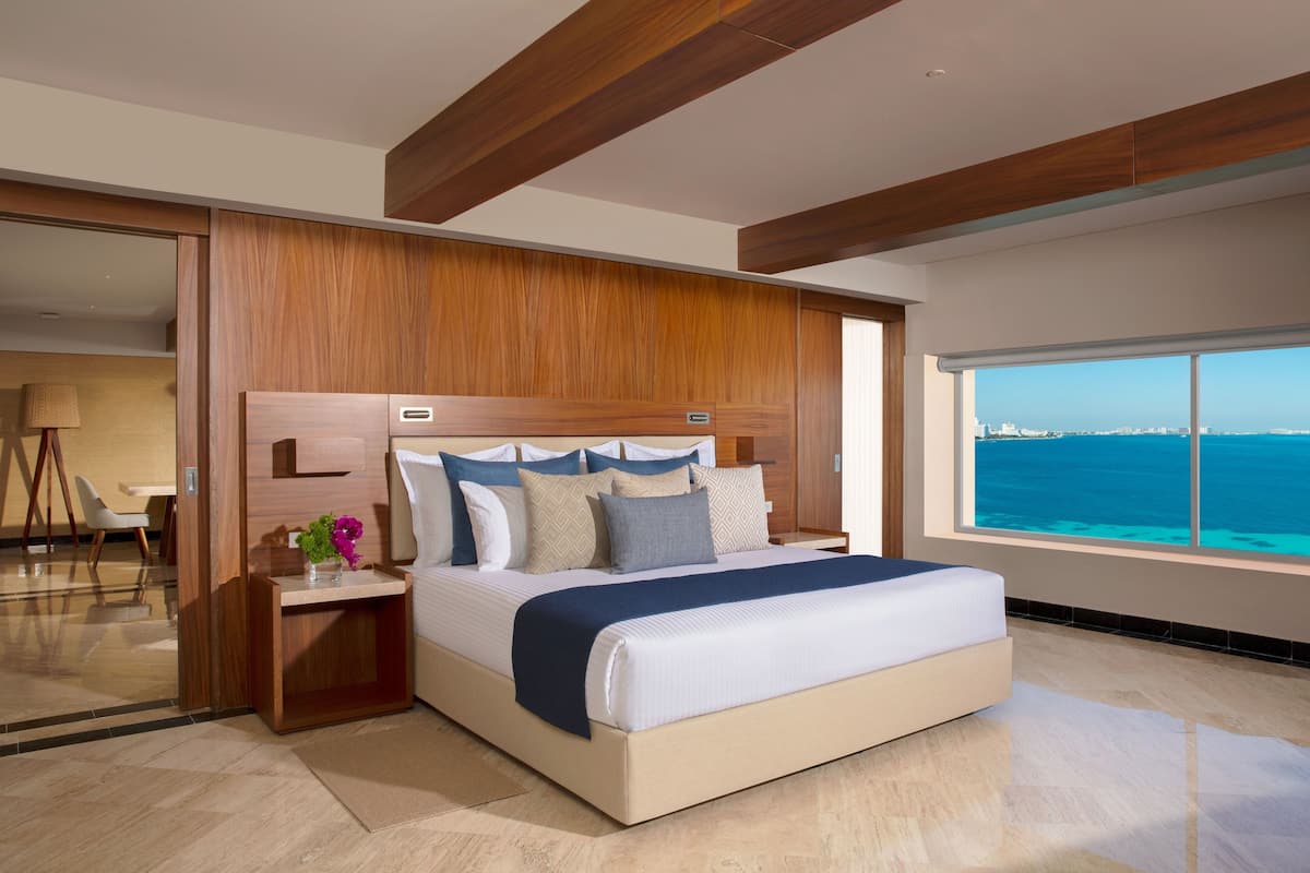 A modern bedroom with a large bed, wooden headboard, and a view of the ocean.
