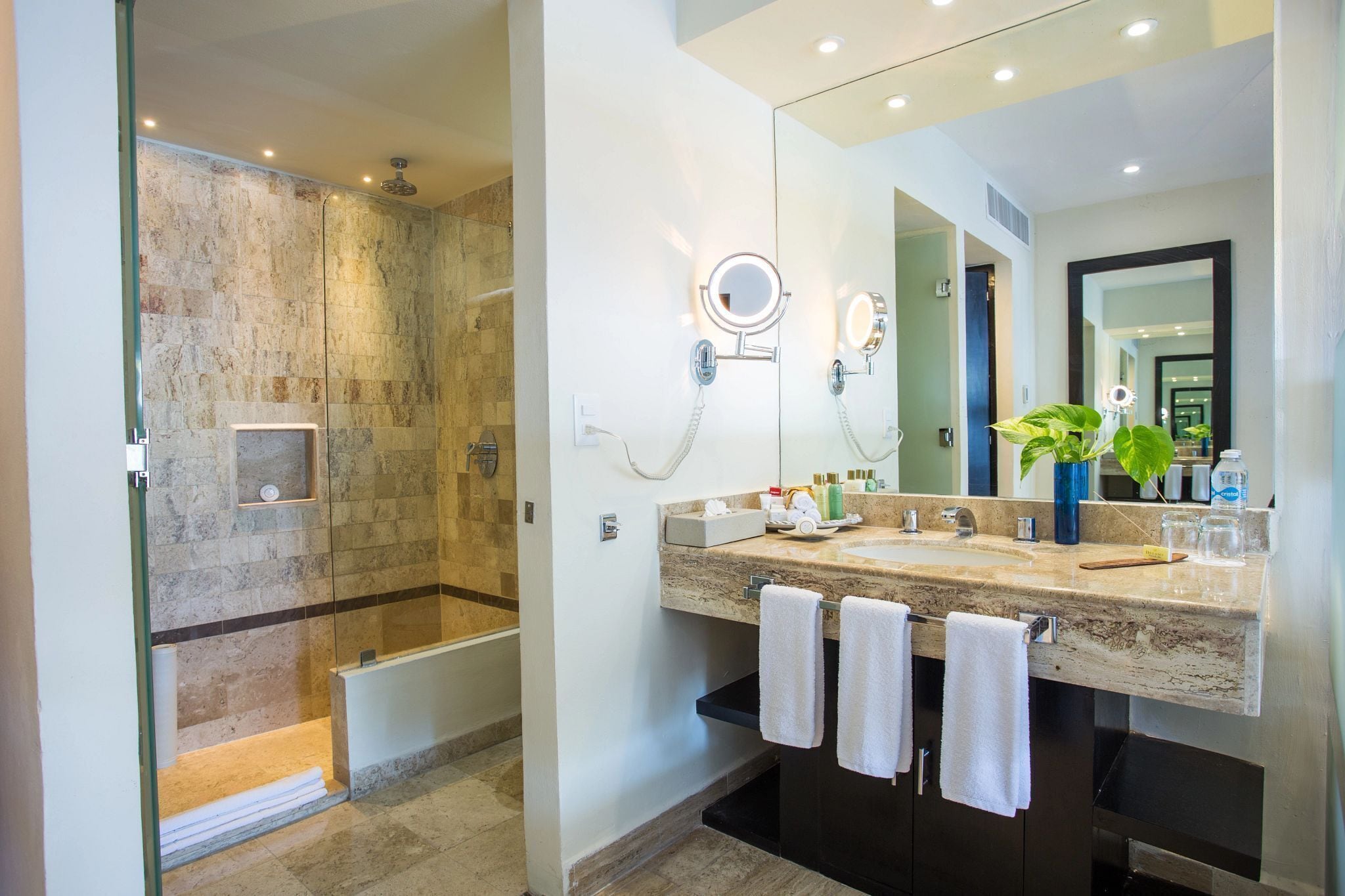 A modern bathroom with a glass-enclosed shower, a large mirror, and a marble countertop.