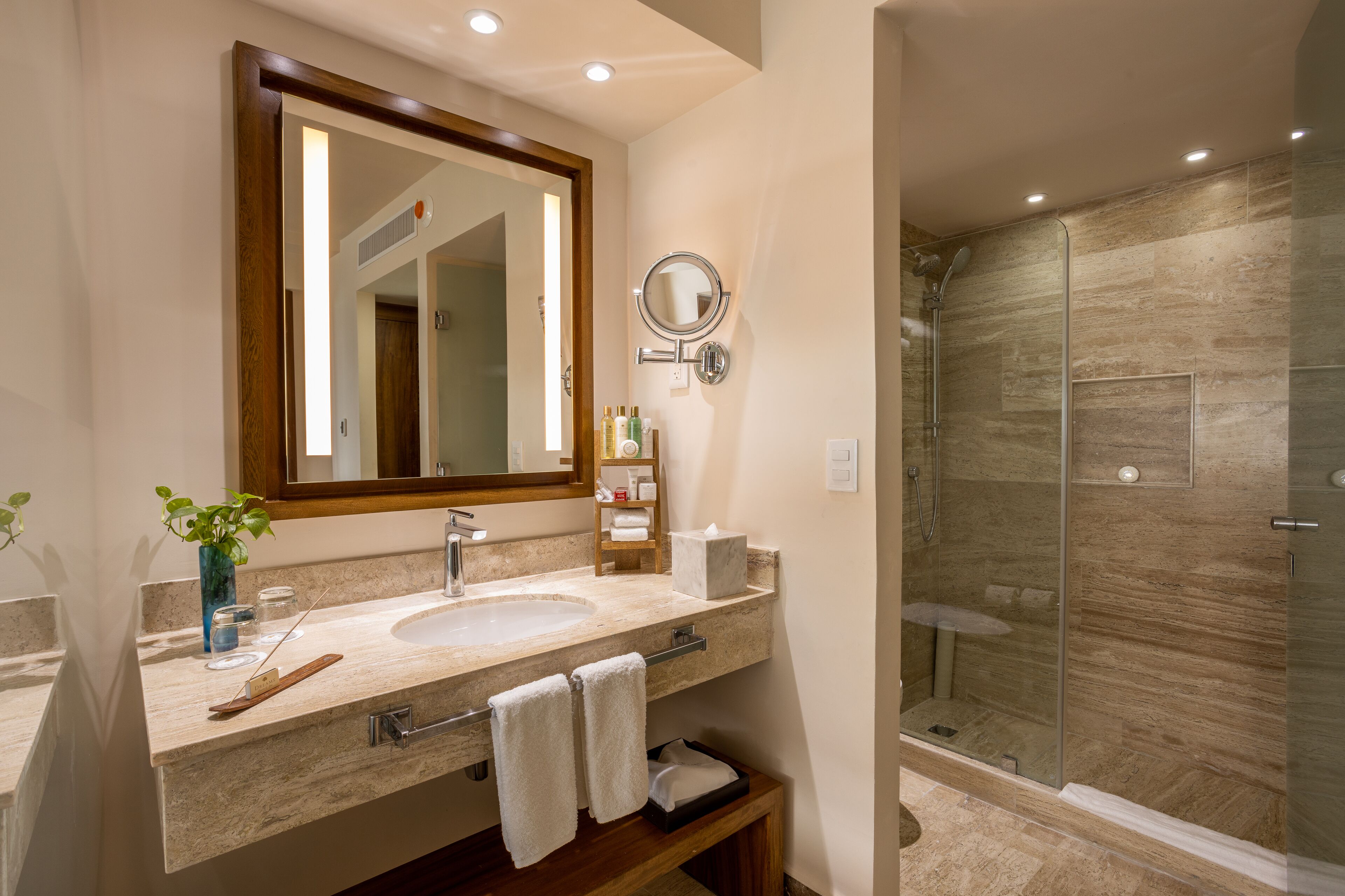 A bathroom with a large mirror, a sink, a glass shower enclosure, and a wooden vanity.