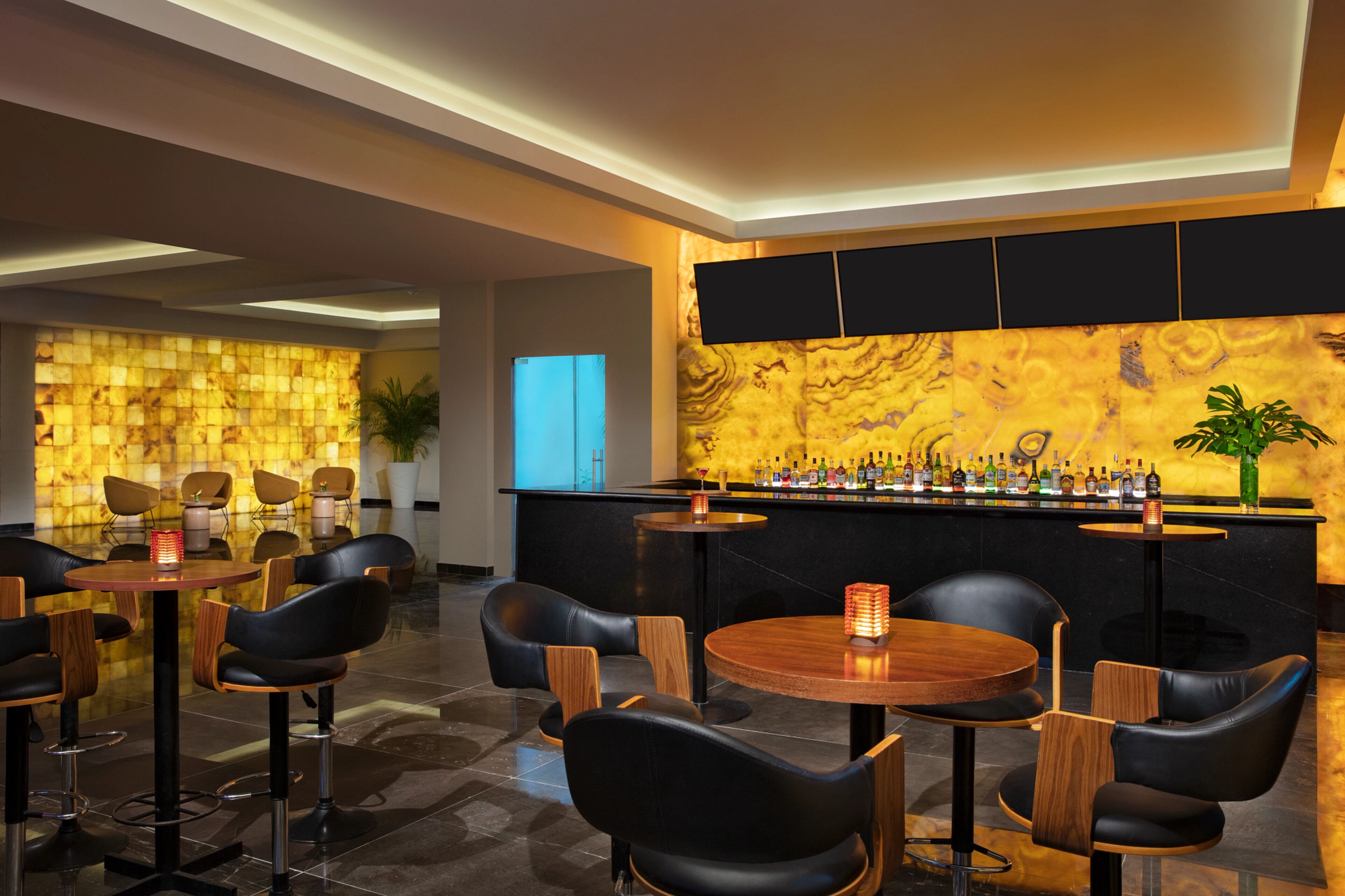 Un área de bar moderna con una pared de mármol, sillas de cuero negro y una variedad de botellas en la barra.