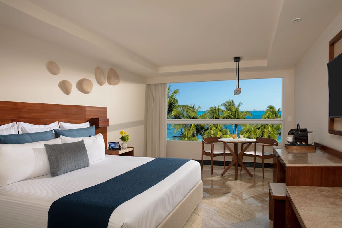 A hotel room with a large bed, a dining area, and a view of the ocean.