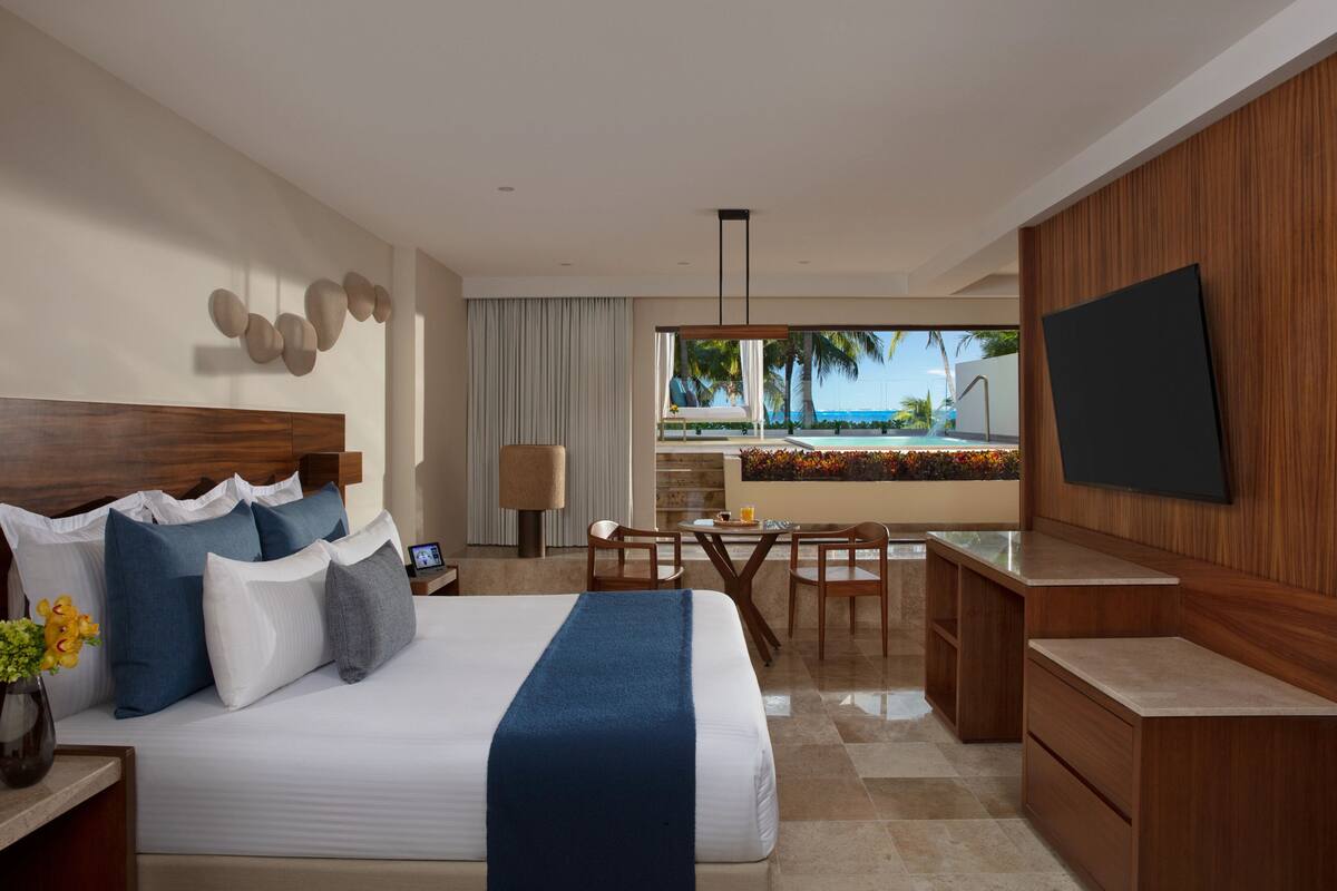 A hotel room with a bed, a desk, a TV, and a view of the beach.