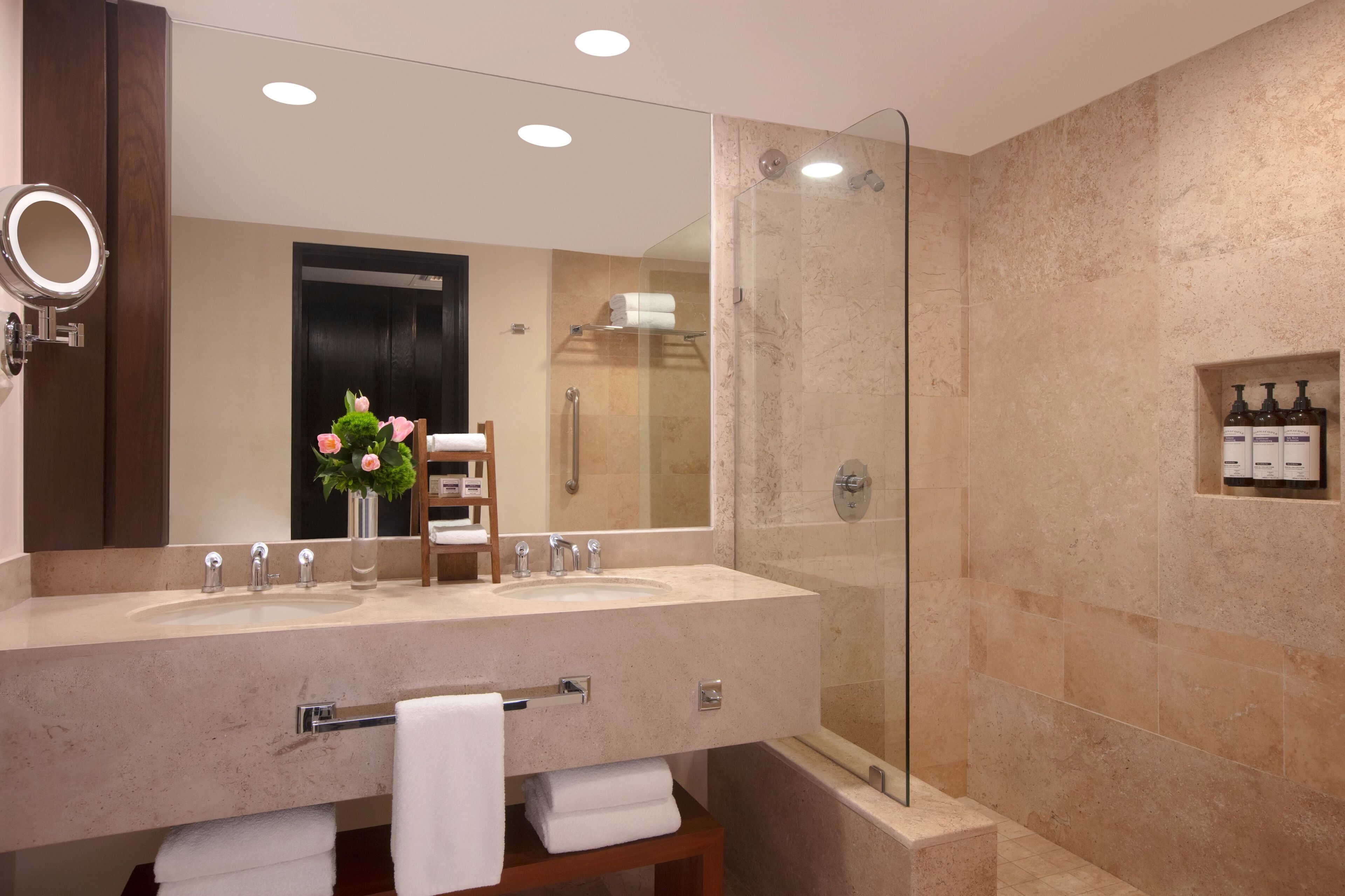A modern bathroom with a large mirror, two sinks, a glass-enclosed shower, and a towel rack.